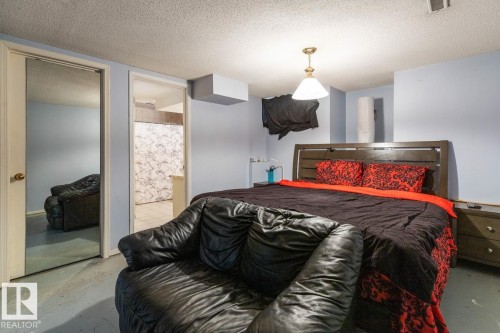 Interior room featuring a wood-finish headboard, light blue walls, a textured ceiling, a ceiling-mounted light fixture, and a mirrored closet door - 4340 33 Street, Edmonton, AB - Indoor Photo Showing Bedroom