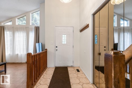 Entryway featuring a white paneled door with decorative glass, tiled flooring, wood railing, and mirrored closet doors - 4340 33 Street, Edmonton, AB - Indoor Photo Showing Other Room