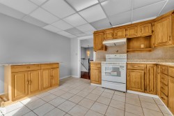 Kitchen featuring oak cabinetry, light-toned tile flooring, a white electric range with hood, and a light-colored countertop - 
