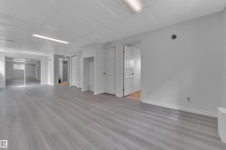 Spacious interior featuring wood-finish flooring, white walls, and a drop ceiling with fluorescent lighting - 