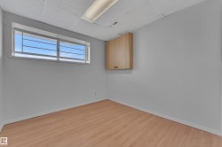Room featuring a wide window with security bars, light wood-finish flooring, light gray walls, a textured ceiling, and an overhead fluorescent light fixture - 