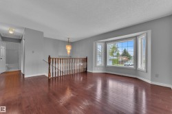 Hardwood flooring throughout the main level, featuring a bay window, chandelier lighting, and a staircase with a wooden railing - 