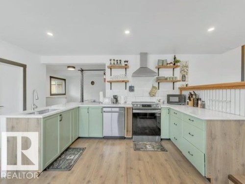 Contemporary kitchen featuring wood-finish flooring, light green cabinetry, white countertops, and a white subway tile backsplash - 3602 50Th Ave, Sylvan Lake, AB - Indoor Photo Showing Kitchen