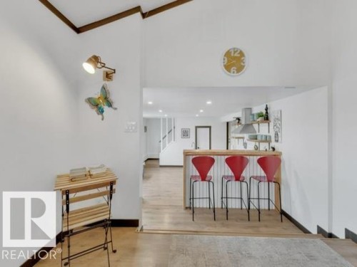 Open-concept interior featuring wood-finish flooring, a breakfast bar with beadboard paneling, and a contemporary wall-mounted light fixture - 3602 50Th Ave, Sylvan Lake, AB - Indoor Photo Showing Other Room