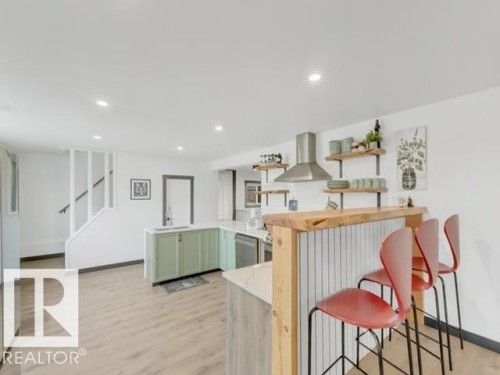 Open-concept kitchen featuring light wood-finish flooring, recessed lighting, a stainless steel range hood, and light green lower cabinetry - 3602 50Th Ave, Sylvan Lake, AB - Indoor