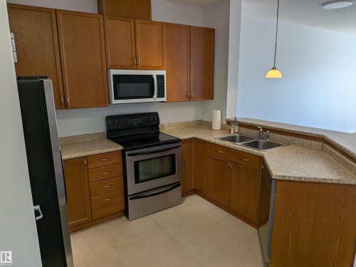 Kitchen featuring wood-finish cabinetry, speckled countertops, and stainless steel appliances including an electric range and built-in microwave - 419 4304 139 Avenue, Edmonton, AB - Indoor Photo Showing Kitchen With Double Sink