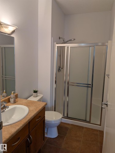 Full bathroom featuring a shower enclosure with sliding glass doors, a white toilet, and a vanity with a laminate countertop, integrated sink, and wood-finish cabinetry - 419 4304 139 Avenue, Edmonton, AB - Indoor Photo Showing Bathroom