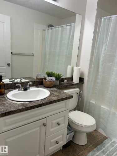 Bathroom featuring a white vanity with panel cabinetry and satin nickel hardware, a dark speckled countertop, an integrated sink, and a full-width mirror - 1228 9363 Simpson Drive, Edmonton, AB - Indoor Photo Showing Bathroom