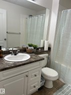 Bathroom featuring a white vanity with panel cabinetry and satin nickel hardware, a dark speckled countertop, an integrated sink, and a full-width mirror - 