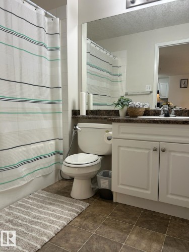 Bathroom featuring a white vanity with paneled doors, a dark stone-finish countertop, and a large wall-mounted mirror - 1228 9363 Simpson Drive, Edmonton, AB - Indoor Photo Showing Bathroom