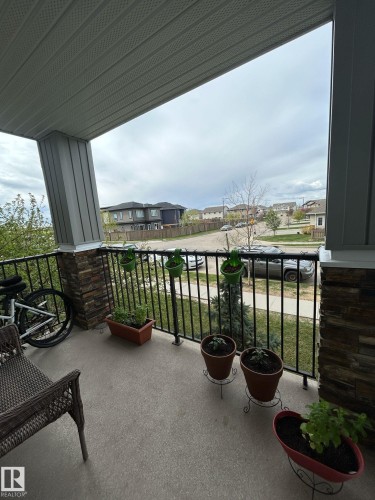 Covered porch with stone column accents, black metal railings, and a textured concrete surface - 1228 9363 Simpson Drive, Edmonton, AB - Outdoor With Exterior