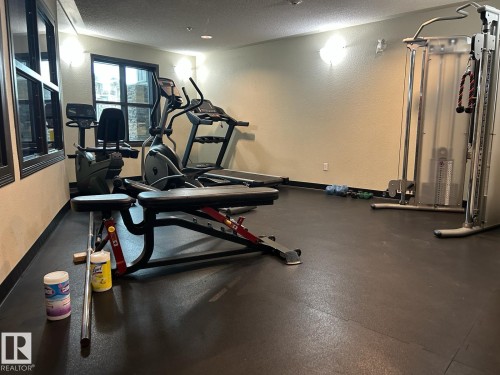 Dedicated fitness space featuring rubber flooring, a large window, wall-mounted light fixtures, and neutral-toned walls - 1228 9363 Simpson Drive, Edmonton, AB - Indoor Photo Showing Gym Room