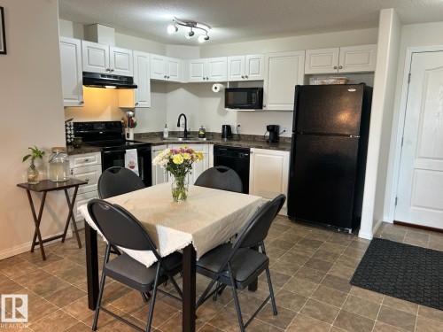 Functional kitchen with white cabinetry, black appliances, and durable tile flooring - 1228 9363 Simpson Drive, Edmonton, AB - Indoor
