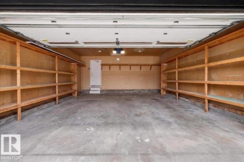 Spacious garage featuring a concrete floor, built-in wooden shelving spanning both side walls, and overhead lighting fixtures - 706 Burley Drive, Edmonton, AB - Indoor Photo Showing Garage