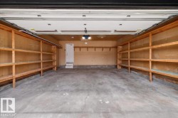 Spacious garage featuring a concrete floor, built-in wooden shelving spanning both side walls, and overhead lighting fixtures - 