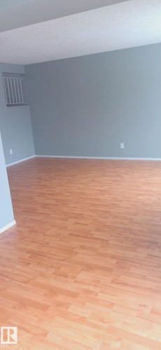 Spacious room featuring wood-finish flooring, light blue wall paint, white baseboards, and a white railing detail - 2554 79 Street, Edmonton, AB - Indoor Photo Showing Other Room