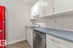 Galley kitchen featuring white cabinetry, light gray countertops, stainless steel sink, and wood-finish flooring - 