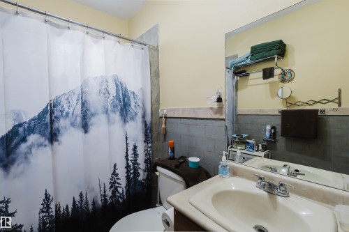 Bathroom featuring a wall-mounted mirror, single vanity with integrated sink, and an adjacent toilet - 10834 75 Avenue, Edmonton, AB - Indoor Photo Showing Bathroom