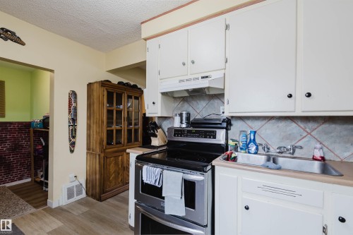 Kitchen featuring white cabinetry, a double basin stainless steel sink, tile backsplash, and wood-finish flooring - 10834 75 Avenue, Edmonton, AB - Indoor Photo Showing Kitchen With Double Sink