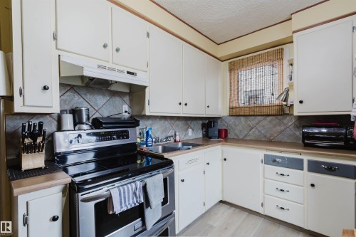 Kitchen featuring white cabinetry, stainless steel range with overhead ventilation, light wood-finish flooring, and a tile backsplash - 10834 75 Avenue, Edmonton, AB - Indoor Photo Showing Kitchen With Double Sink