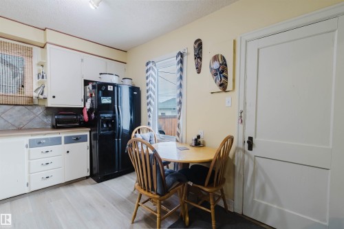 Kitchen featuring light wood-finish flooring, white cabinetry with grey drawer accents, a black side-by-side refrigerator, and a tiled backsplash - 10834 75 Avenue, Edmonton, AB - Indoor
