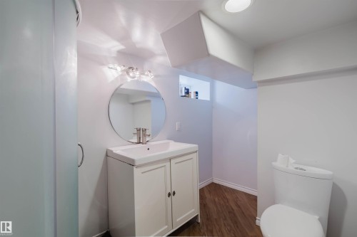 Bathroom featuring a white vanity with integrated sink, circular mirror, and modern wall-mounted light fixture - 10834 75 Avenue, Edmonton, AB - Indoor Photo Showing Bathroom