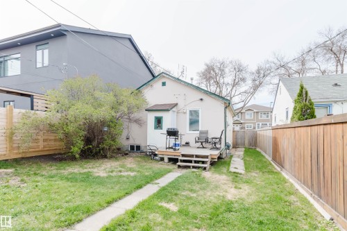 Expansive backyard featuring a manicured lawn, a concrete pathway, a wooden deck, and a modern privacy fence - 10834 75 Avenue, Edmonton, AB - Outdoor