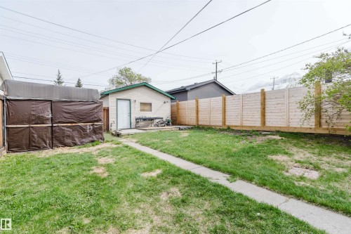 Expansive backyard featuring a concrete pathway, detached garage with vinyl siding, and a wooden privacy fence - 10834 75 Avenue, Edmonton, AB - Outdoor