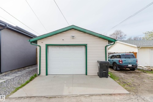 Detached single-car garage featuring a white overhead door, cream siding, green trim, and a concrete apron - 10834 75 Avenue, Edmonton, AB - Outdoor With Exterior
