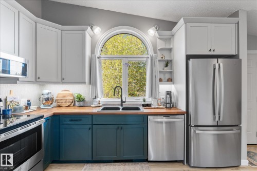 Kitchen featuring an arched window, wood-finish countertops, two-tone cabinetry, a stainless steel refrigerator, and a built-in dishwasher - 4759 48 Street, Onoway, AB - Indoor Photo Showing Kitchen With Double Sink