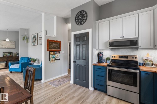 Kitchen featuring light wood-finish flooring, two-tone cabinetry with white upper and blue lower cabinets, light wood countertops, and a stainless steel oven with an above-range microwave - 4759 48 Street, Onoway, AB - Indoor Photo Showing Kitchen