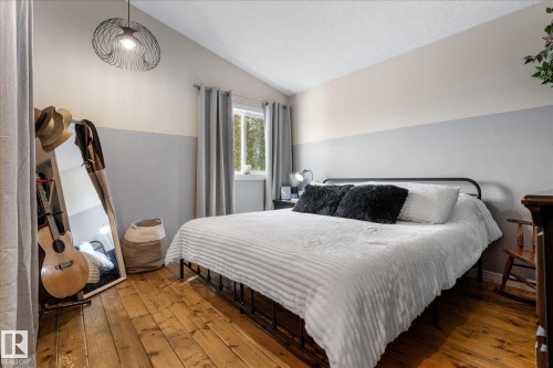 Bedroom featuring wood-finish flooring, a window with grey curtains, and a two-tone painted wall - 4759 48 Street, Onoway, AB - Indoor Photo Showing Bedroom