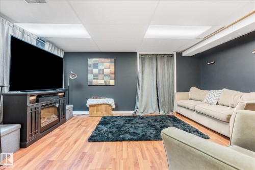 Recreation room featuring wood-finish flooring, dark accent walls, and a drop ceiling with integrated lighting panels - 4759 48 Street, Onoway, AB - Indoor With Fireplace
