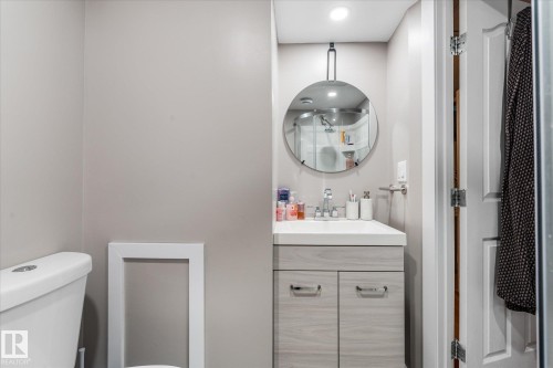 Bathroom featuring a vanity with a light wood-finish cabinet, white countertop, and a round mirror with an overhead light fixture - 4759 48 Street, Onoway, AB - Indoor Photo Showing Bathroom