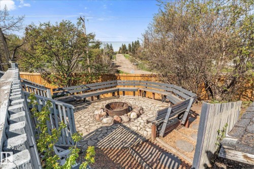 Outdoor fire pit area featuring a stone patio, built-in curved benches, and a wooden privacy fence - 4759 48 Street, Onoway, AB - Outdoor