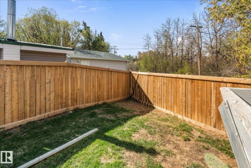 Spacious backyard featuring a new wood privacy fence, a natural grass area, and mature trees in the background - 4759 48 Street, Onoway, AB - Outdoor