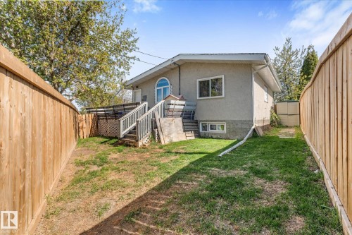 Rear property exterior with a stucco finish, featuring a wooden deck with railing, arched window, and a lower-level window - 4759 48 Street, Onoway, AB - Outdoor With Exterior