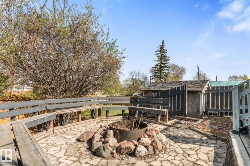 Stone patio featuring a central fire pit surrounded by a built-in wooden bench - 4759 48 Street, Onoway, AB - Outdoor With Deck Patio Veranda
