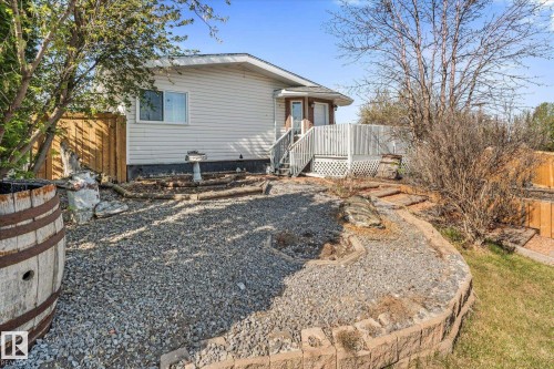 Rear exterior featuring white vinyl siding, a multi-level deck with white railing, and a gravel patio area - 4759 48 Street, Onoway, AB - Outdoor