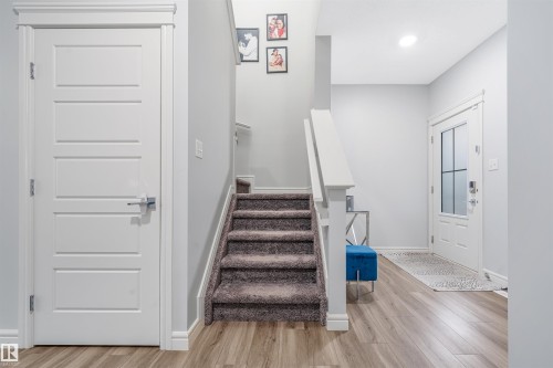 Foyer featuring wood-finish flooring, a carpeted staircase with white railings, a modern paneled interior door, and a front entry door with frosted glass inserts - 1024 Daniels Loop, Edmonton, AB 