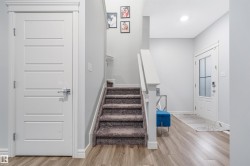 Foyer featuring wood-finish flooring, a carpeted staircase with white railings, a modern paneled interior door, and a front entry door with frosted glass inserts - 