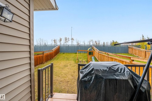 Backyard featuring a wooden deck with black metal railings, a sloped lawn, and a wooden privacy fence - 1024 Daniels Loop, Edmonton, AB 