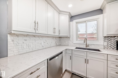 Modern kitchen featuring white shaker-style cabinetry with brushed nickel hardware, light-toned countertops, a stainless steel dishwasher, a single-basin sink with a gooseneck faucet, and a subway tile backsplash - 4006 115 Avenue, Edmonton, AB 