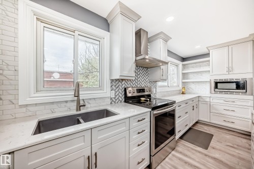 Bright kitchen featuring white shaker cabinetry, stainless steel appliances, quartz countertops, and wood-finish flooring - 4006 115 Avenue, Edmonton, AB 