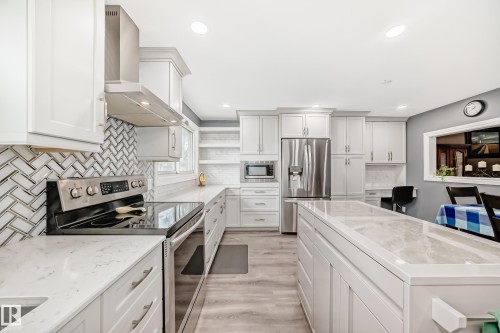 Kitchen featuring white shaker cabinetry, stainless steel appliances, herringbone tile backsplash, light-toned countertops, and wood-finish flooring - 4006 115 Avenue, Edmonton, AB 