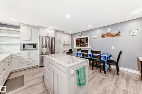 Modern kitchen featuring white cabinetry, stainless steel appliances, a center island with a light-toned countertop, and wood-finish flooring - 4006 115 Avenue, Edmonton, AB 