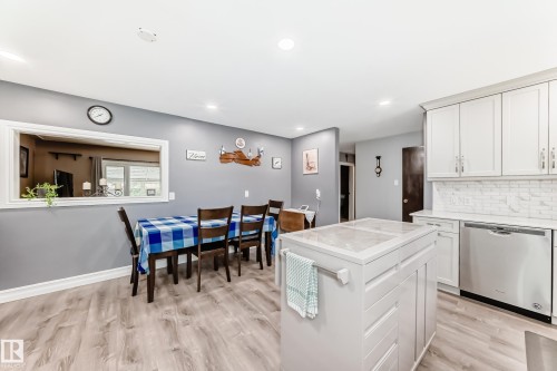 Open-concept kitchen and dining area featuring light wood-finish flooring, white cabinetry, a subway tile backsplash, and a central island with a solid surface countertop - 4006 115 Avenue, Edmonton, AB 