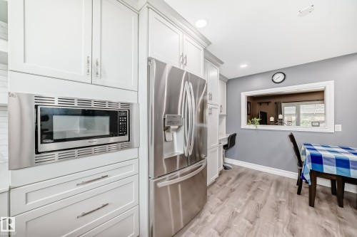 Contemporary kitchen featuring white cabinetry with silver hardware, a built-in stainless steel microwave, and a stainless steel refrigerator - 4006 115 Avenue, Edmonton, AB 