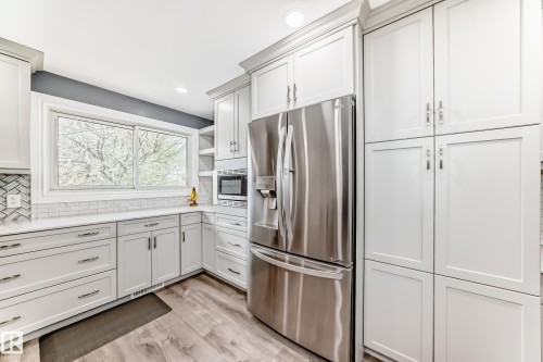 Modern kitchen featuring white shaker cabinetry, stainless steel appliances, wood-finish flooring, recessed lighting, and a white subway tile backsplash - 4006 115 Avenue, Edmonton, AB 