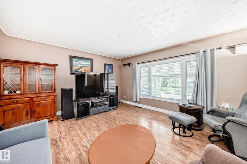 Bright living space featuring wood-finish flooring, a large bay window with white trim, and neutral wall tones - 4006 115 Avenue, Edmonton, AB 